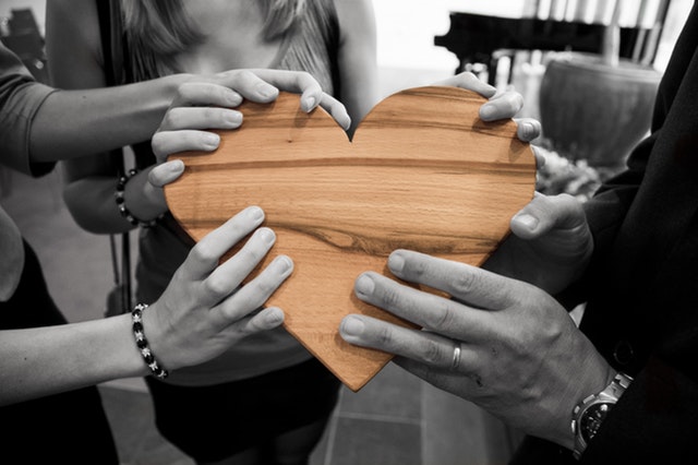 People holding heart made of wood in hands