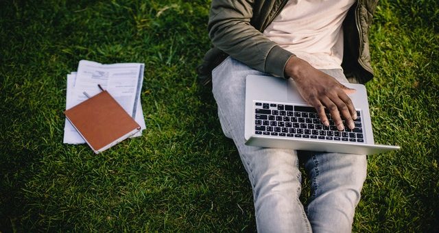 A guy sitting on grass taking online classes from a tutor